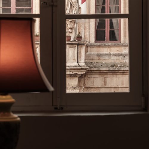 A warm photo of a lampshade in the Presidential Suite of The Xara Palace Relais & Chateaux overlooking the magnificent facade of the Mdina Local Council which housed the Maltese Law Courts in the past